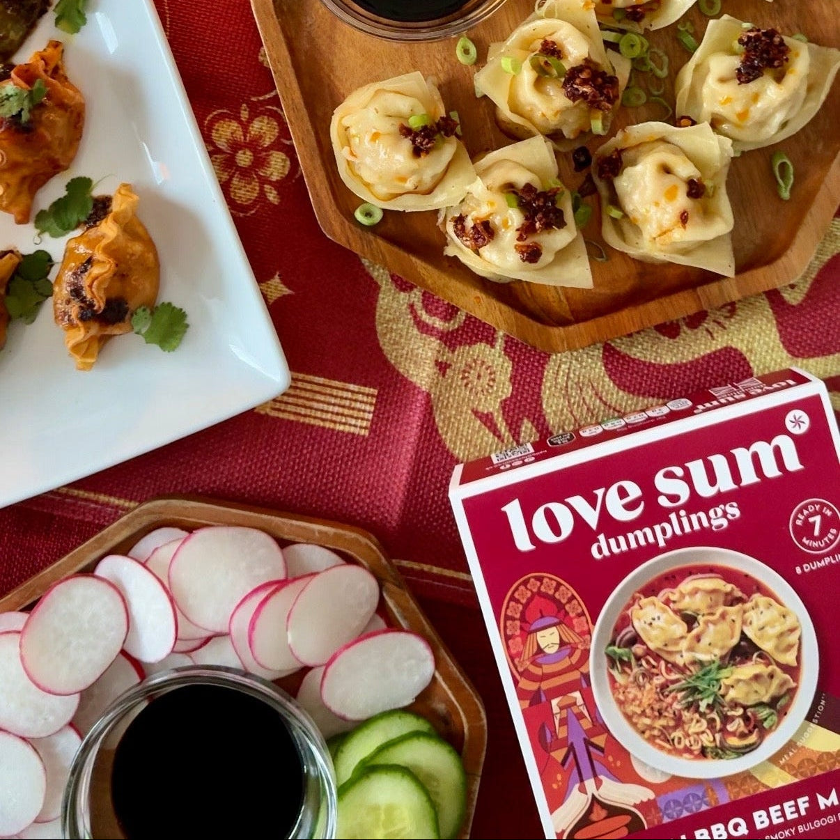 Dumplings on a wooden tray with 'love sum' packaging and a candle on a red tablecloth.