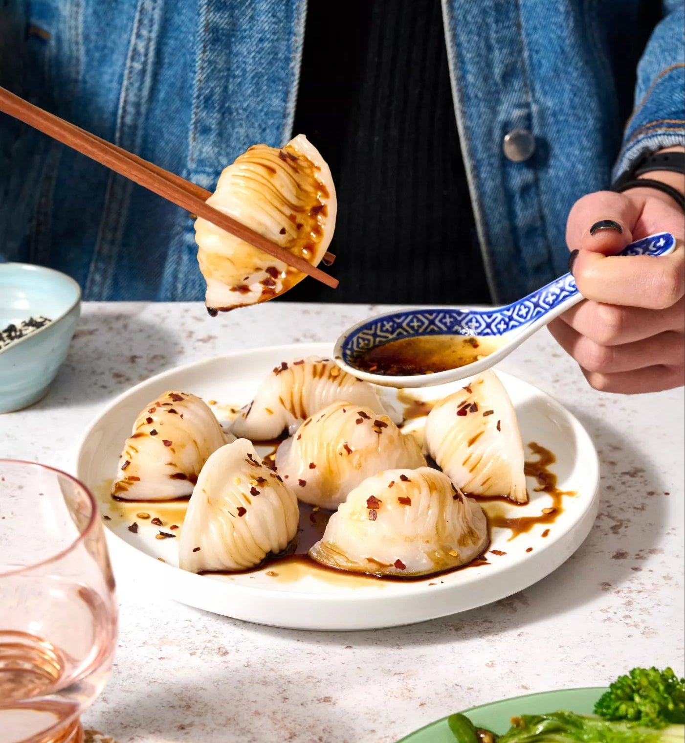 Person eating dumplings with chopsticks and a spoon, surrounded by plates of food on a table.
